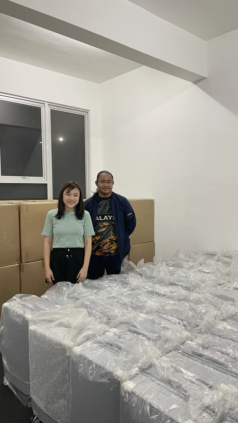 Two people from Al-Waqar Travel in front of their order, rows of wrapped cases stacked in a hall